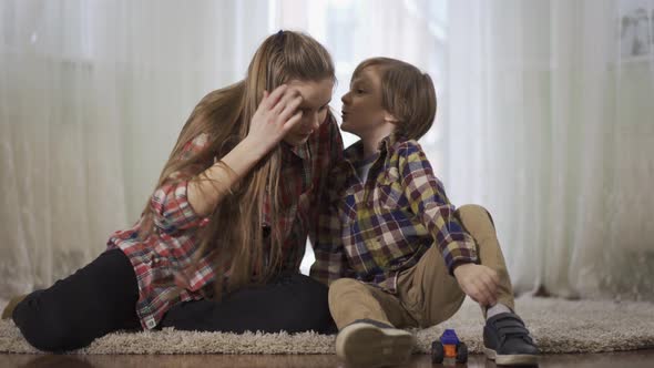 Older Sister and Younger Brother Playing Together Sitting on the Floor on the Fluffy Carpet. The Boy