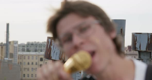 Young Rocker Guy with Glasses is Expressively Singing with Grimace Using Golden Microphone on Stand