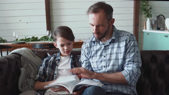 Father and son sitting on couch reading book