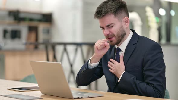 Sick Young Businessman with Laptop Coughing in Office 