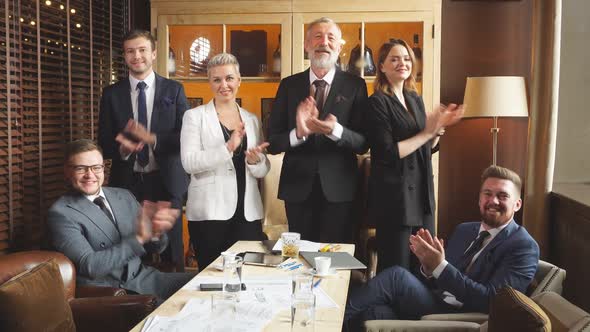 Office Staff Standing Behind Wooden Table Smiling Cheerfully Rising in Applause in Front of Camera