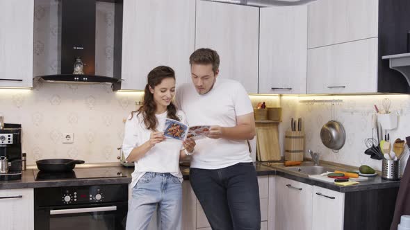 Couple Discussing Reading Recipe Book Choosing Dish for Dinner at Home Kitchen