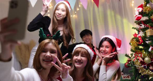 Group of happy Asian friends taking selfie with smartphone in Christmas night party at home.