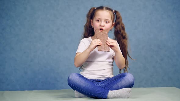 Girl sitting on the table and eating chocolate. Girl eating chocolate bar