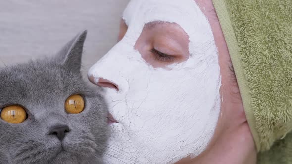 Woman in a Mask of White Clay on Face Holds a British Cat in Arms