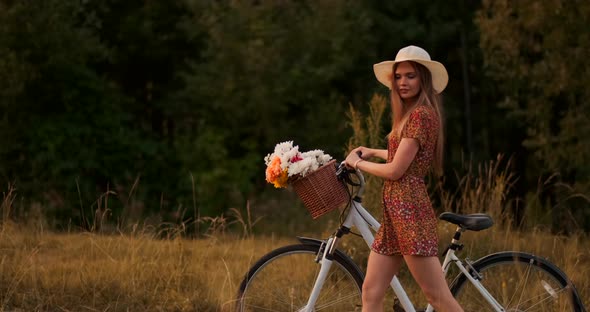 Side View Smiling Girl in a Dress Walking with a Bike in the Summer on the Handlebar Basket with