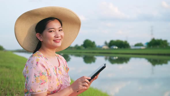 Portrait of beautiful asian woman with hat looking at camera using portable device.