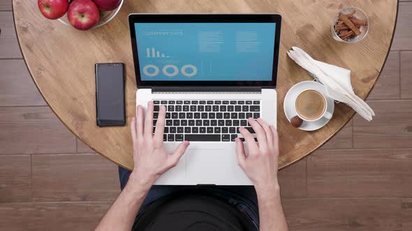 Top View: Man Sitting at a Wooden Table Looks at Company Data