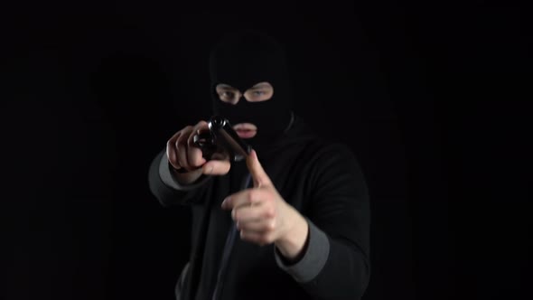 A Man in a Balaclava Mask Stands with a Gun. A Thug Points His Gun at the Camera. On a Black