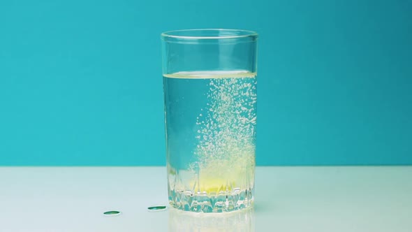 Close-up Shot of An Effervescent Yellow Pill Against Pain Falls Into a Glass and Dissolves