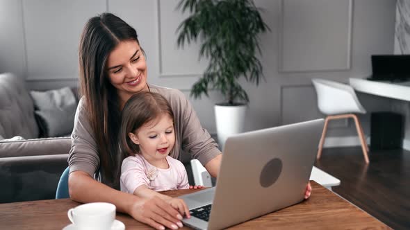 Happy Mother and Cute Little Daughter Surfing Internet on Laptop