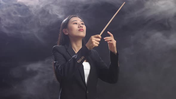 Asian Conductor Woman Holding A Baton And Showing Gesture Quickly In The Black Studio With Fog