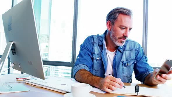 Male executive using mobile phone while working at desk