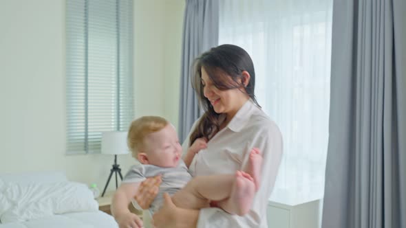 Caucasian loving mom play with cute baby boy child on bed in bedroom in the morning at house. alt