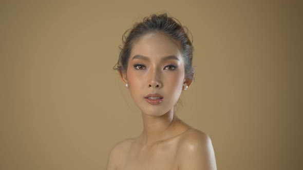 Beautiful young Asian woman posing for glamour headshots in a professional fashion shoot with beige