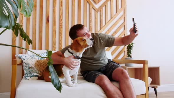 A Joyful Young Man Sitting at Table and Taking Selfie with Pet Using Phone