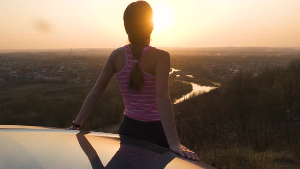 Young Woman Standing Near Her Car Enjoying Warm Sunset View