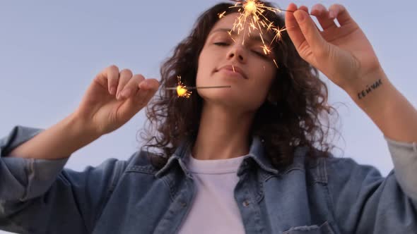 A young woman with sparklers is dancing and celebrating a holiday outside. Fireworks, bengal lights