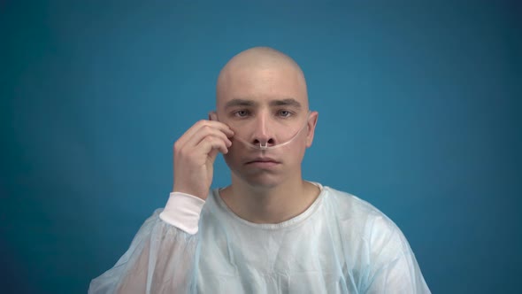 A Bald Young Man with Oncology Sadly Looks at the Camera on a Blue Background. The Patient