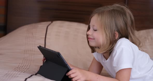 A Little Girl Lying on a Sofa Scrolls a Tablet