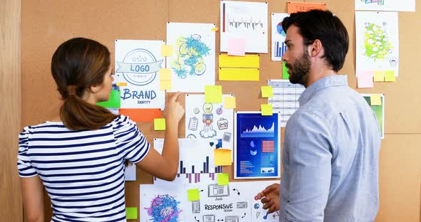 Male and female executives discussing over bulletin board