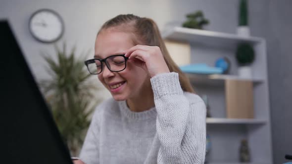 Attractive Happy Smiling Teen Girl in Glasses Reading the Funny Text on Laptop Screen