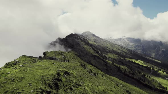 Aerial drone shot flying along grass covered mountains with a small trail leading along. More green