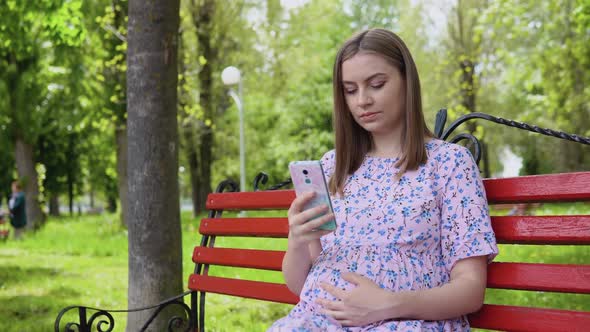 A Pregnant Woman is Sitting in a Summer Park and Reading Information for Pregnant Women on a
