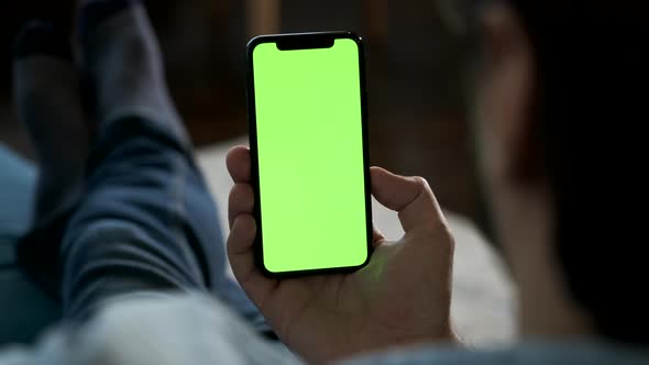 Close-Up of a Man's Hand Holding a Smartphone with a Green Screen looking At and Showing a New App