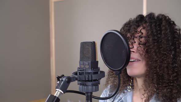 A Fashionable Energetic Singer Sings Into a Microphone in a Recording Studio