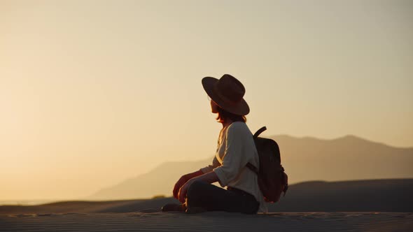 Attractive girl in a hat in lotus position at sunset