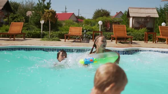 Young Caucasian Girl with Water Pistol and Inflatable Tubes Jumping Into Pool While Another Kids