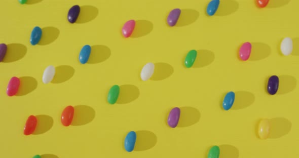 Video of overhead view of rows of multi coloured sweets over yellow background