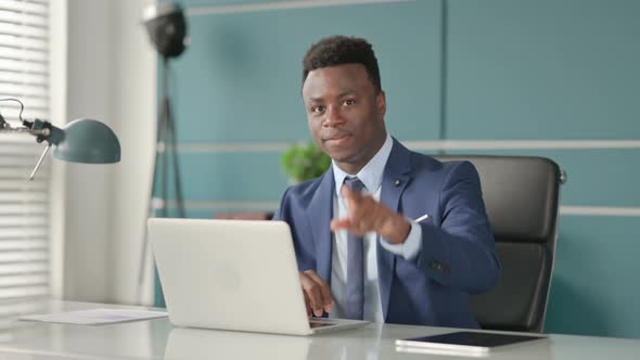 African Businessman Pointing at Camera While Using Laptop in Office