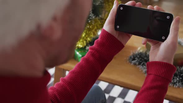 Happy albino african american man wearing santa hat using smartphone at christmas