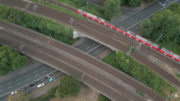 Birds eye view of a railway bridge crossing a big street with a red commuter train crossing the brid