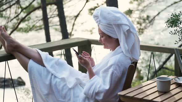 Young Woman in a Bathrobe and Towel on the Terrace on the Background of Mountains and Forests