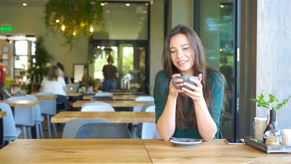 Young Woman Sitting in a Cafe Outdoor Drinking Coffee. Portrait of Happy Girl with Cup of Coffee