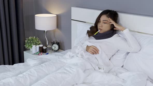 sick woman using thermometer to checking her temperature and her headache in bed