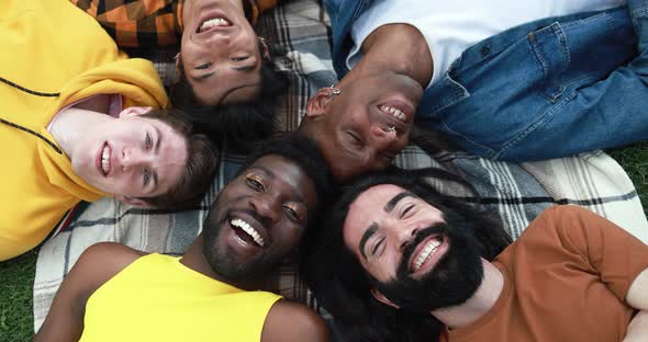 Group of multiracial male friends lying on park meadow smiling on camera - Happy diverse people