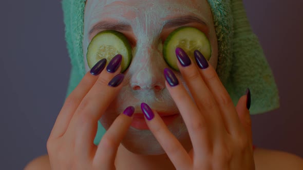 Woman with Mask on Face Holds Cucumber Slices on Eyes