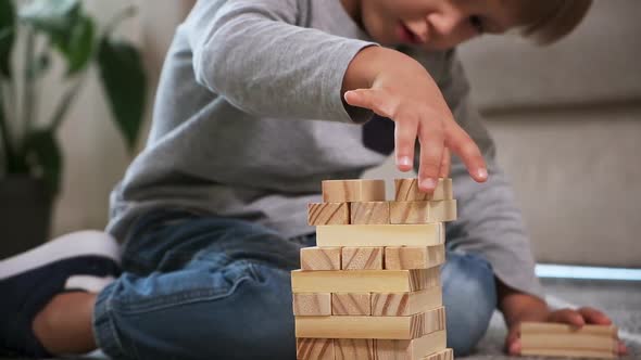 Child Builds a Wooden Tower for Playing with Wooden Blocks Sitting on the Floor at Home