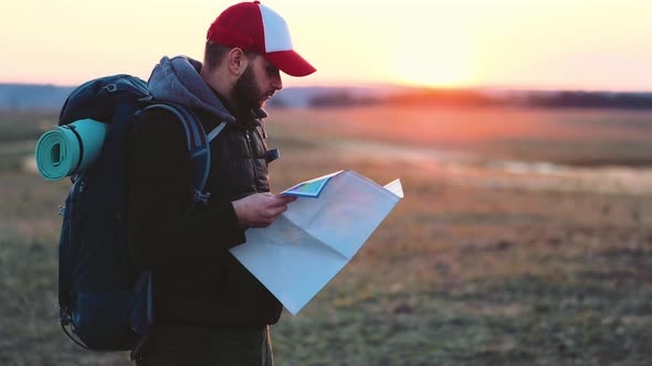 Adventure Man with Map and Extreme Explorer Gear on Mountain with Sunset