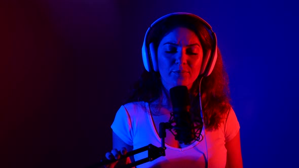 Caucasian Woman in Headphones Sings Into a Microphone in Neon Light