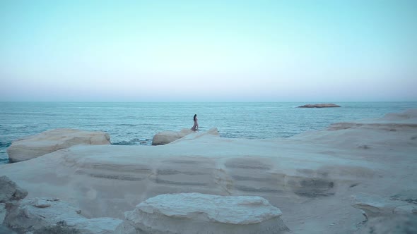Woman Walks Along the Coastline on the Rocks