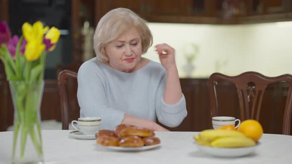 Lonely Senior Woman Sitting at Table Sighing Waiting for Children