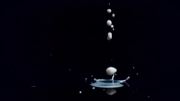 Drops of milk on black surface against black background. Slow Motion.