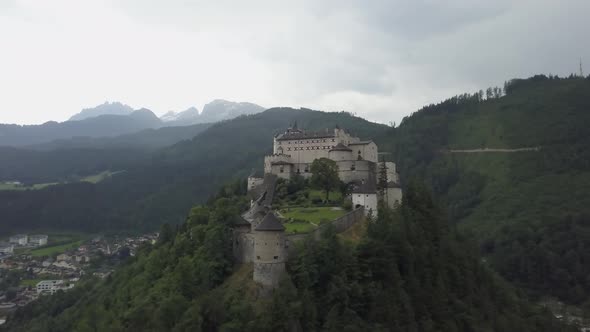 Aerial orbit of medieval Hohenwerfen Fortress on top of a steep hill, surrounded by pine forest and