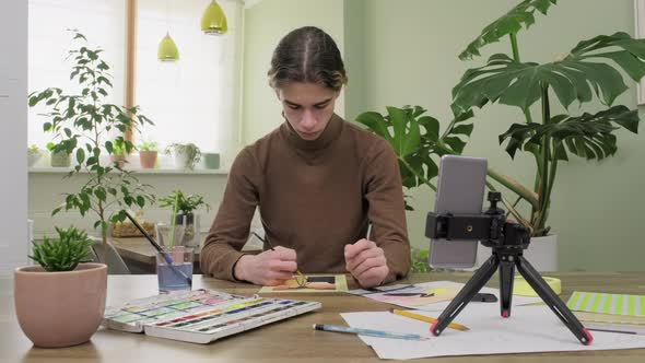 Teenage Guy Drawing with Watercolors Watching Video Class on Smartphone