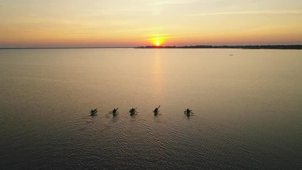 Five Kayaks with People are Sailing Towards the Sunrise